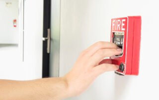 person reaching out to fire alarm inside school for fire damage prevention tips for schools