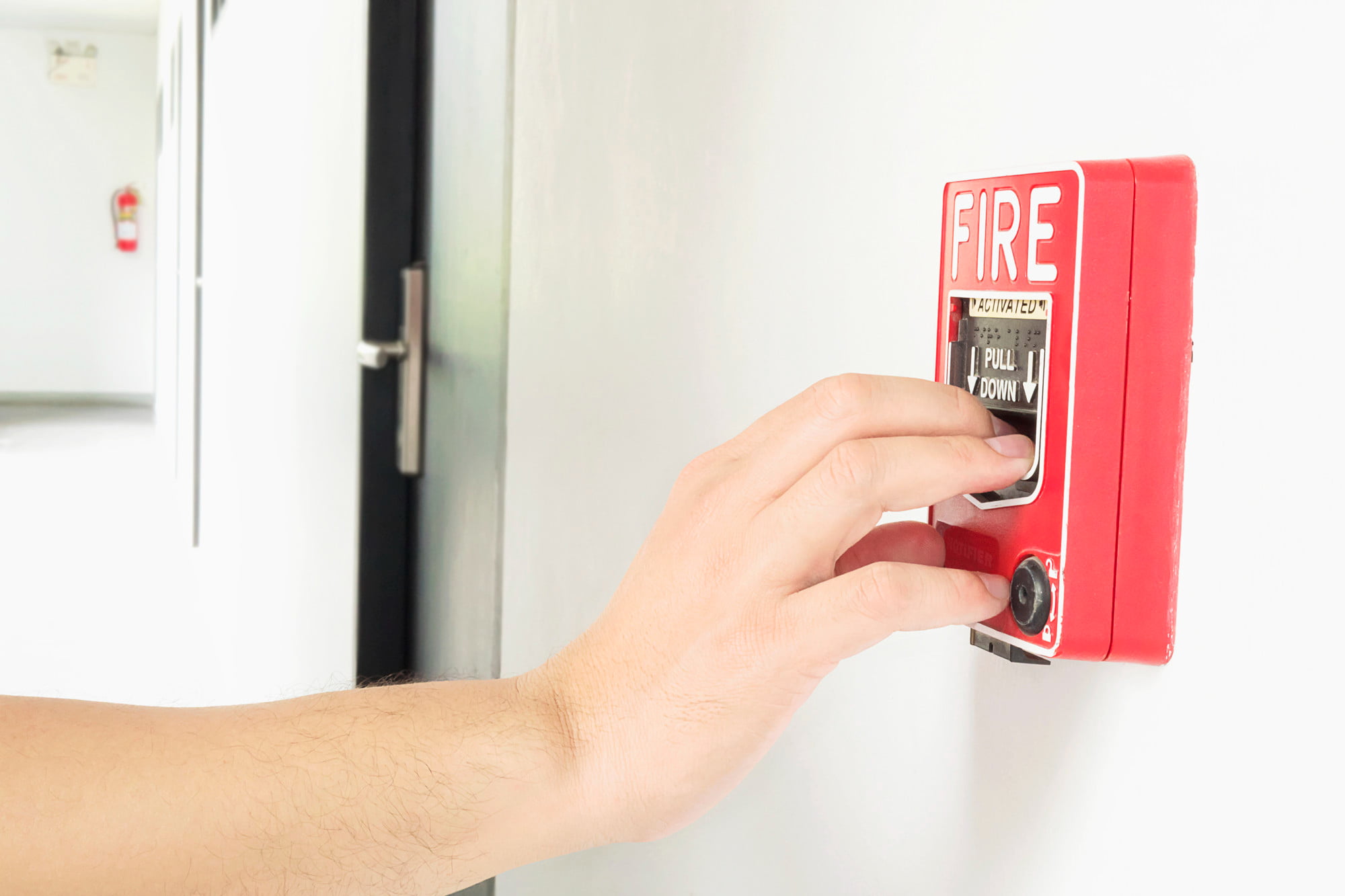 person reaching out to fire alarm inside school for fire damage prevention tips for schools