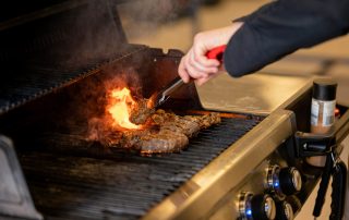 close up of hand grilling safely using top fire safety tips for BBQ season