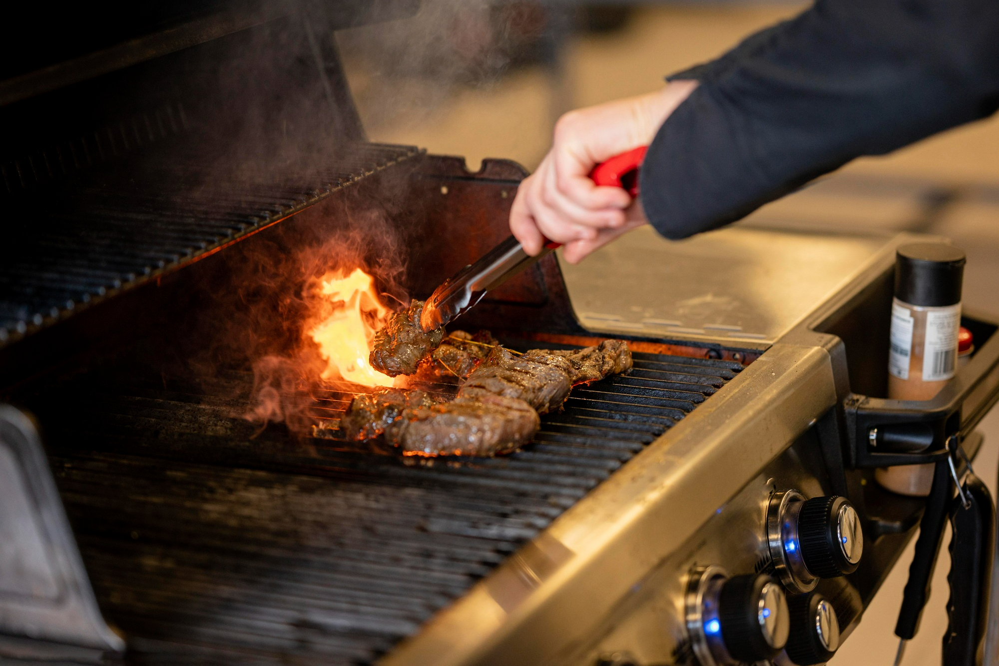 close up of hand grilling safely using top fire safety tips for BBQ season