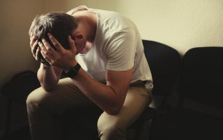 man-holding-his-head-in-his-hands-while-sitting-on-a-couch-struggling-with-PTSD-and-home-fires